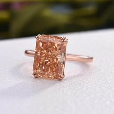 a pink diamond ring sitting on top of a white surface with greenery in the background