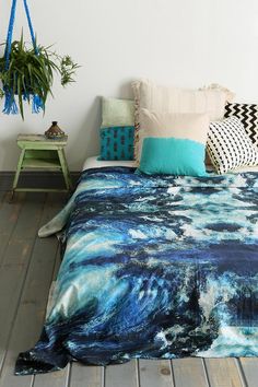 a bed covered in blue and white pillows next to a potted plant on top of a wooden floor