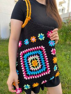 a woman is holding a crocheted bag in her hands while standing on the grass