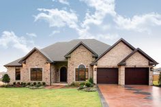 a brick and stone house in the middle of a grassy area with two garages