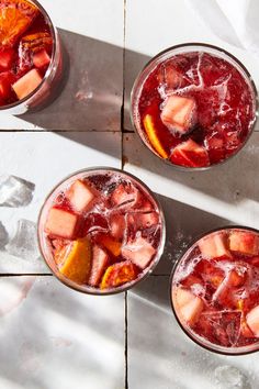 three glasses filled with drinks sitting on top of a white tile floor next to each other