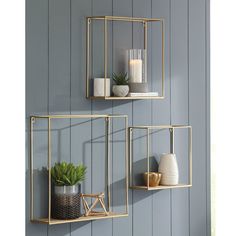 two gold metal shelves with plants and candles on them, against a blue painted wall