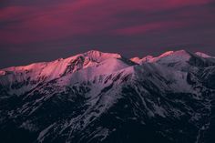 the mountains are covered in snow under a pink and purple sky with clouds above them