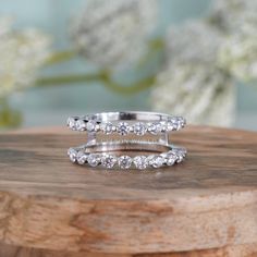 two wedding rings sitting on top of a wooden table with flowers in the back ground