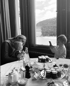 two children sitting at a table with food and drinks in front of them, looking out the window