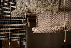 several pieces of woven material hanging from hooks on a wall next to a window with bamboo blinds