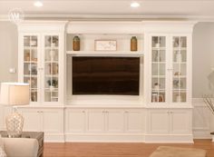 a living room with white built in cabinets and a flat screen tv mounted on the wall