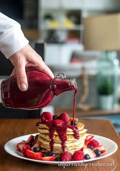 a person pouring syrup onto a stack of pancakes