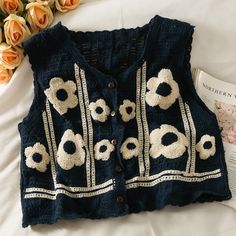 a blue sweater with white flowers on it and a book next to it that is laying on a bed