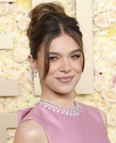 a woman in a pink dress smiling at the camera with flowers behind her and an embellishment on her face