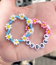 a hand holding a beaded bracelet with letters and flowers