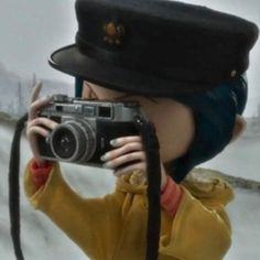 a woman taking a photo with a camera in the snow wearing a hat and coat