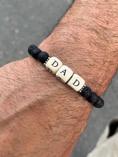 These bracelets are a fun combination of squared letter beads spelling out the word DAD, surrounded by silver Bali spacers and black lava beads.  They are a simple but still elegant piece perfect as a gift for the great dads for Father's Day or any day.  Fits mens wrist approx. 7 1/4" ONLY AVAILABLE IN SIZE LISTED Casual Black Beads Wristband Gift, Customized Bracelets For Father's Day, Casual Wristband With Letter Beads As Gift, Casual Letter Print Jewelry For Gifts, Father's Day Gift Jewelry With Letter Beads, Black Beaded Bracelets With Letter Print As Gift, Masculine Bracelets For Father's Day Gift, Black Beaded Bracelet With Letter Print As Gift, Father’s Day Beaded Bracelet