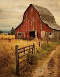 an old red barn sits on the side of a dirt road