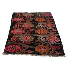 a black rug with red, orange and pink flowers on the bottom is laying on a white surface