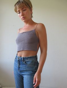 a woman standing in front of a white wall wearing jeans and a cropped top