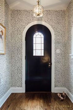 an entryway with a black door and white wallpaper on the walls, along with wooden flooring