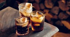 three glasses filled with different types of drinks on top of a wooden table next to firewood