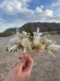 a hand holding a hair comb with flowers and feathers on it in front of mountains