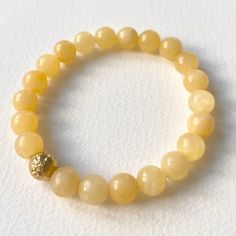 A 24ct gold plated brass pearl with a rustic surface is hidden among the pastel yellow minerals of the Honey Calcite Bracelet, giving it a special overall effect. In addition to the pleasant harmony of colors, honey calcite offers benefits such as energizing and boosting self-confidence.  The bracelet consists of 22 pearls, and thanks to its flexible design, it fits perfectly on an average female wrist.  The bracelet is handmade in our Budapest studio. MATERIAL: 24 carat gold-plated brass, honey Elegant Amber Beaded Bracelets With Natural Stones, Elegant Amber Beaded Bracelets, Elegant Hand-strung Amber Bracelets, Yellow Hand-strung Jewelry For Meditation, Elegant Hand-strung Amber Bracelet, Gold Bracelets With Natural Round Beads, Gold Bracelets With Round Natural Stones, Gold Agate Bracelet With Gemstone Beads, Gold Citrine Gemstone Bracelets