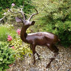 a statue of a deer is in the middle of some flowers and bushes with rocks