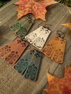 six wooden earrings with designs on them sitting on a table next to leaves and grass