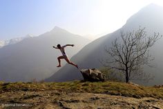 a man jumping off a cliff into the air with mountains in the backgroud