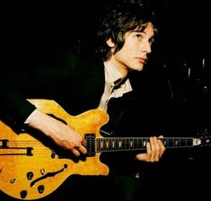 a young man playing an electric guitar in front of a black background with his hand on the neck