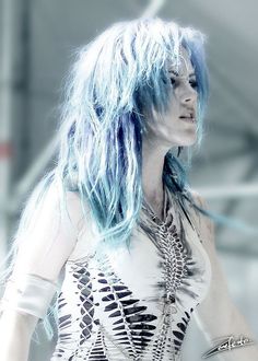 a woman with blue hair and piercings on her chest standing in front of a building