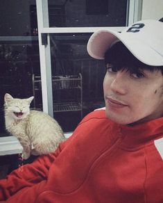 a person wearing a baseball cap with a cat in front of them on a window sill