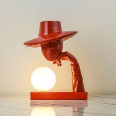 a red hat on top of a table next to an orange light bulb in the shape of a person's head