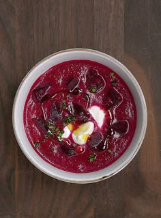 a white bowl filled with beet soup on top of a wooden table next to a spoon