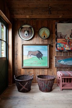 two baskets are sitting on the floor in front of a wall with pictures and paintings