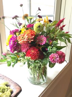 a vase filled with lots of colorful flowers on top of a window sill in front of a window