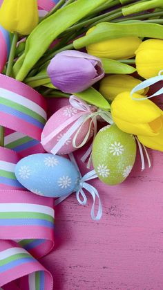 colorful easter eggs, tulips and ribbons on pink wood background with copy space