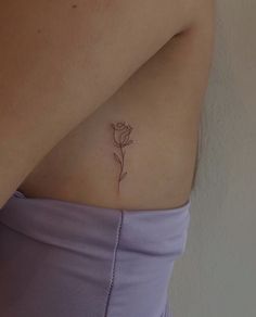 a woman's stomach with a single flower tattoo on her left side ribcage