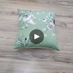 a green pillow with pink flowers on it sitting on a wooden floor next to a video player