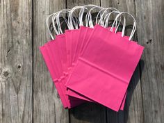 pink paper bags are lined up on a wooden surface with white handles and strings attached to them