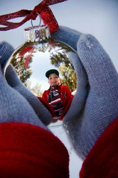 a person holding a christmas ornament in their hands with the reflection of them