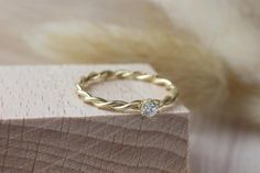 a yellow gold ring with a diamond on it sitting on top of a wooden block