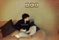 a young man sitting on top of a couch holding a nintendo wii game controller