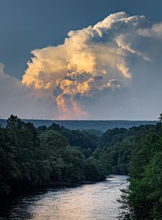 the sun is shining through some clouds over a river and trees in the foreground