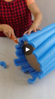 a woman cutting up blue towels on top of a white table with an orange handled knife