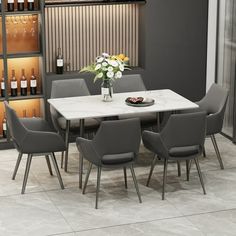 a dining room table with grey chairs and wine bottles on the shelves in the background