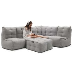 a woman sitting on top of a gray couch next to a foot stool and ottoman