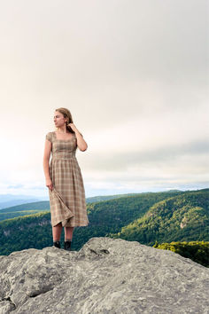 Girl standing on a mountain top with a plaid dress on. Brown Fitted Plaid Dress, Fitted Brown Plaid Dress, Fall Plaid Dress With Short Sleeves, Fitted Brown Plaid Dress For Spring, Fitted Plaid Midi Dress For Daywear, Fall Gingham Plaid Midi Dress, Fall Plaid Midi Dress, Fitted Brown Plaid Dress For Fall, Casual Brown Dress For Picnic