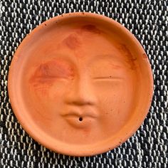 a clay plate with a face painted on the front and sides, sitting on a woven surface