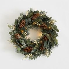 a christmas wreath with pine cones, greenery and lights on the front door or wall