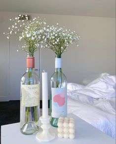 two bottles with flowers in them sitting on a table next to a candle and some marshmallows