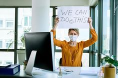 a woman wearing a face mask holds up a sign that says we can do this